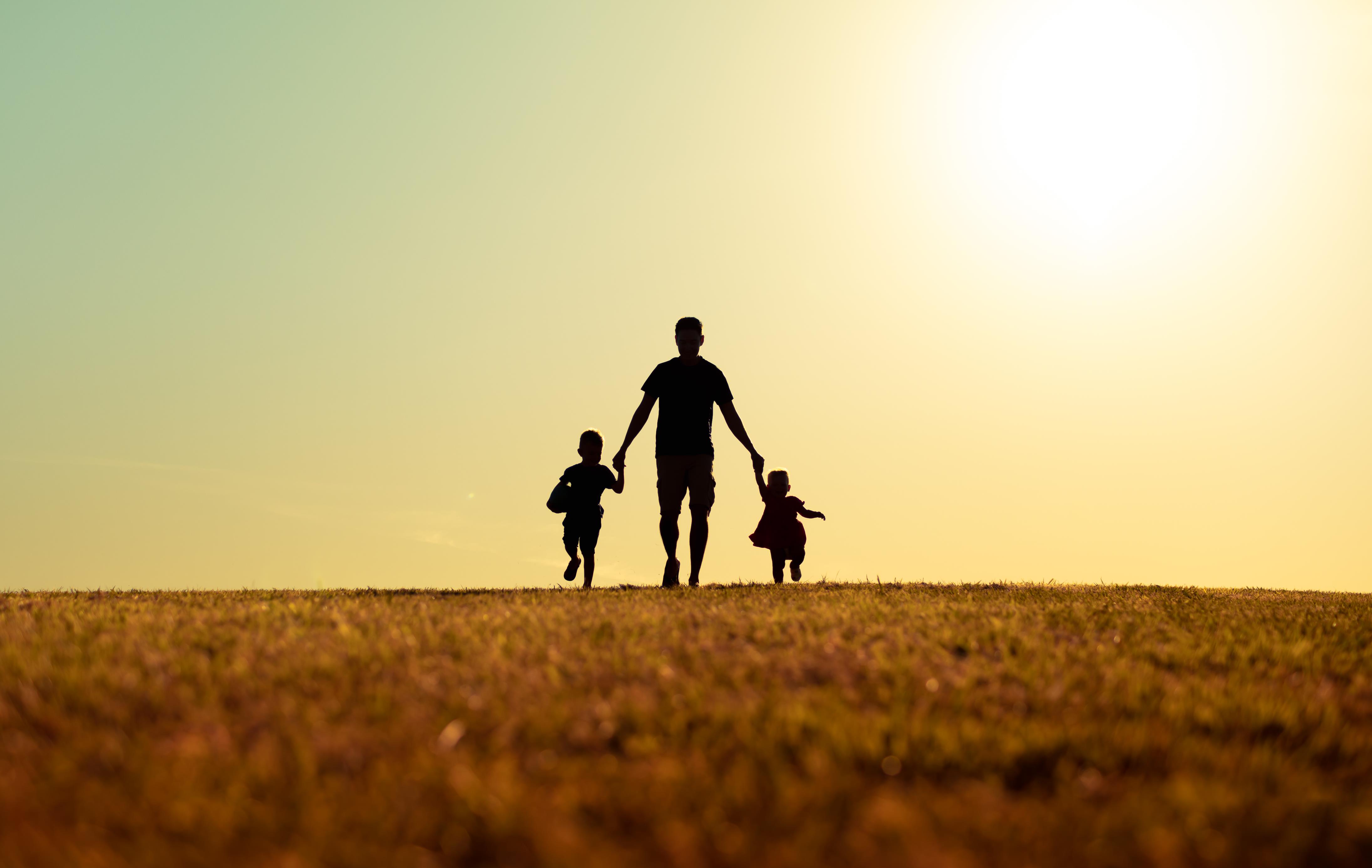 Silhouette of a father walking with son and daughter in park at sunset.