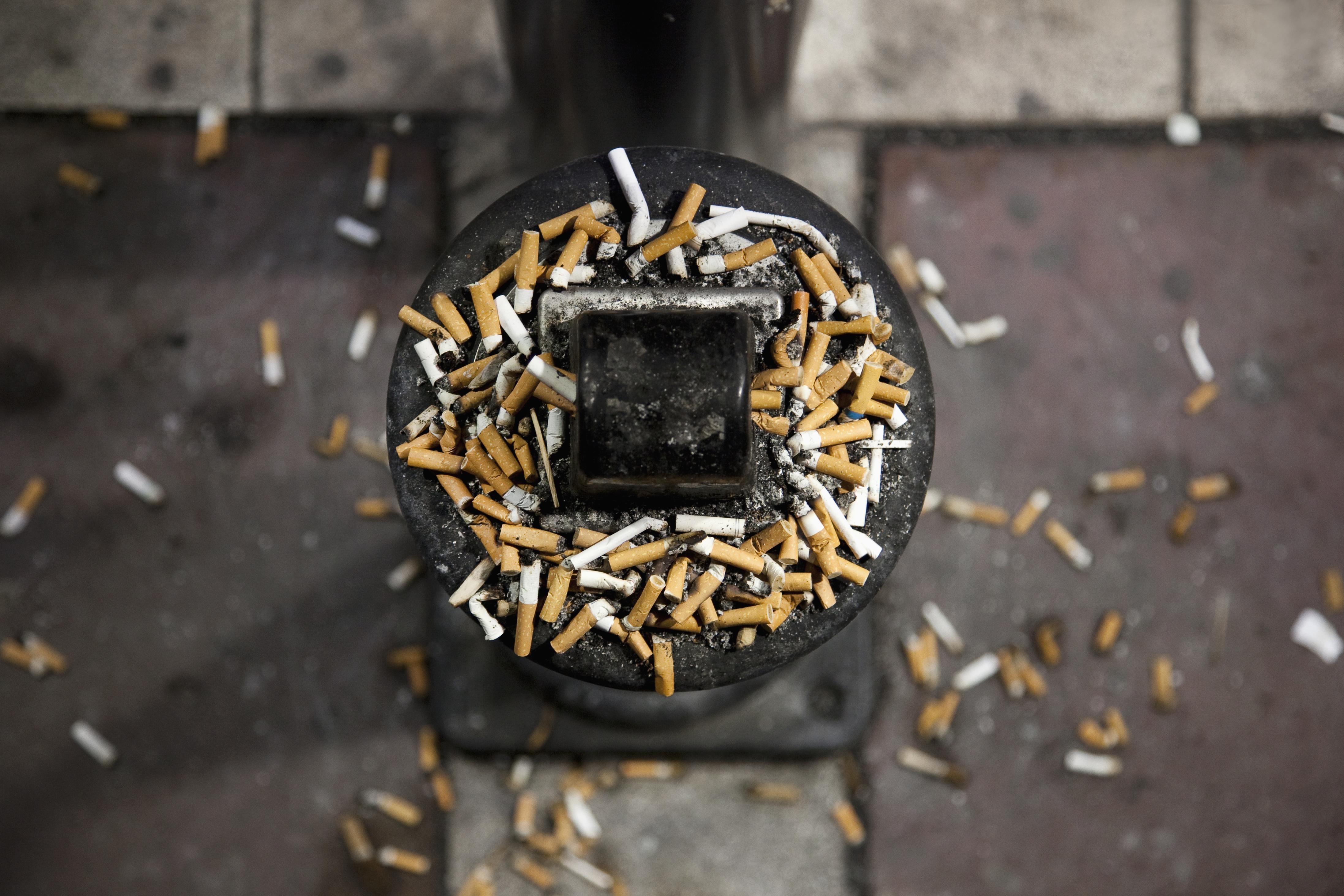 Cigarette butts spilling out of an outdoor ashtray and o<em></em>nto the ground around it.