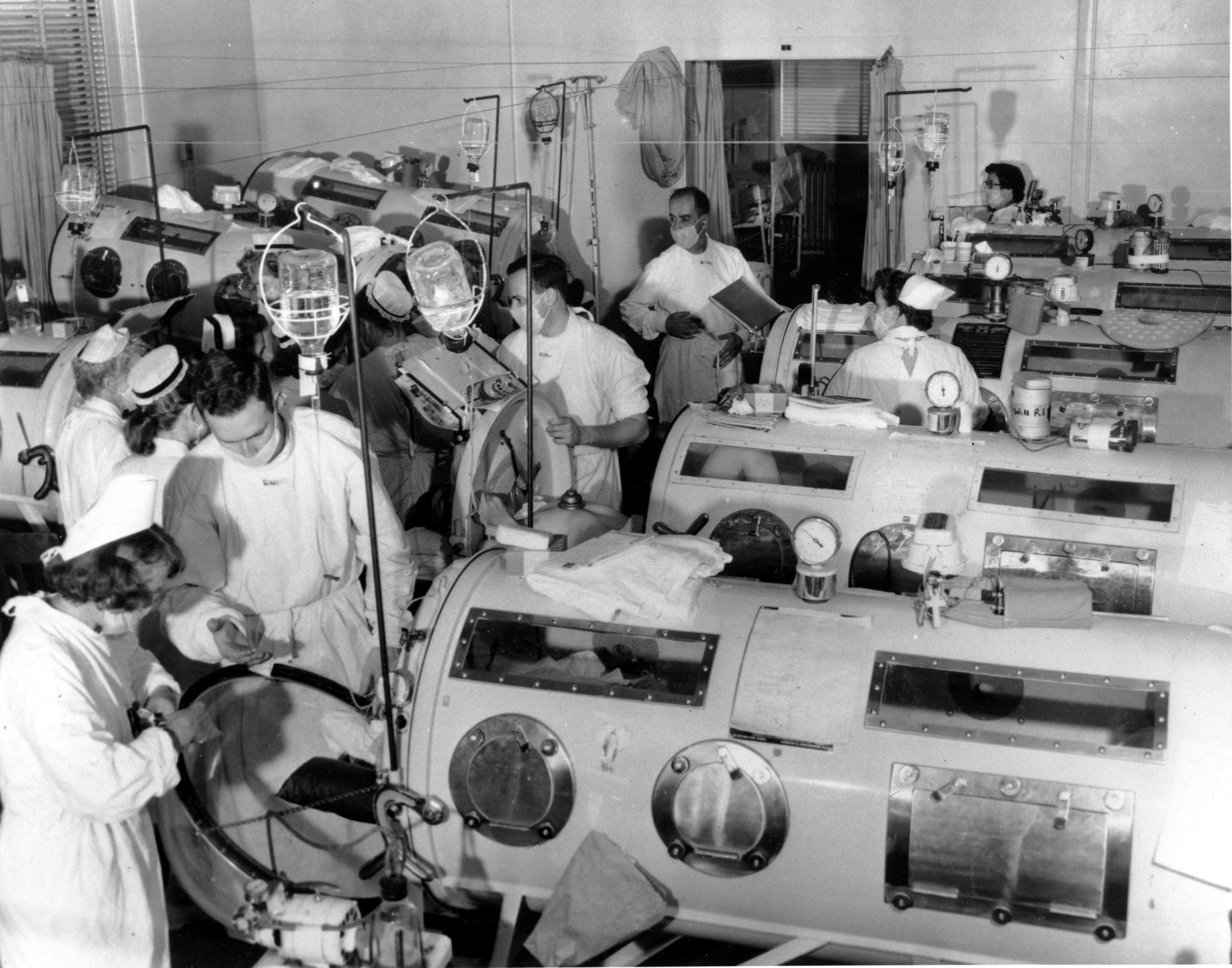 Critical-care patients are lined up close together in iron lung respirators