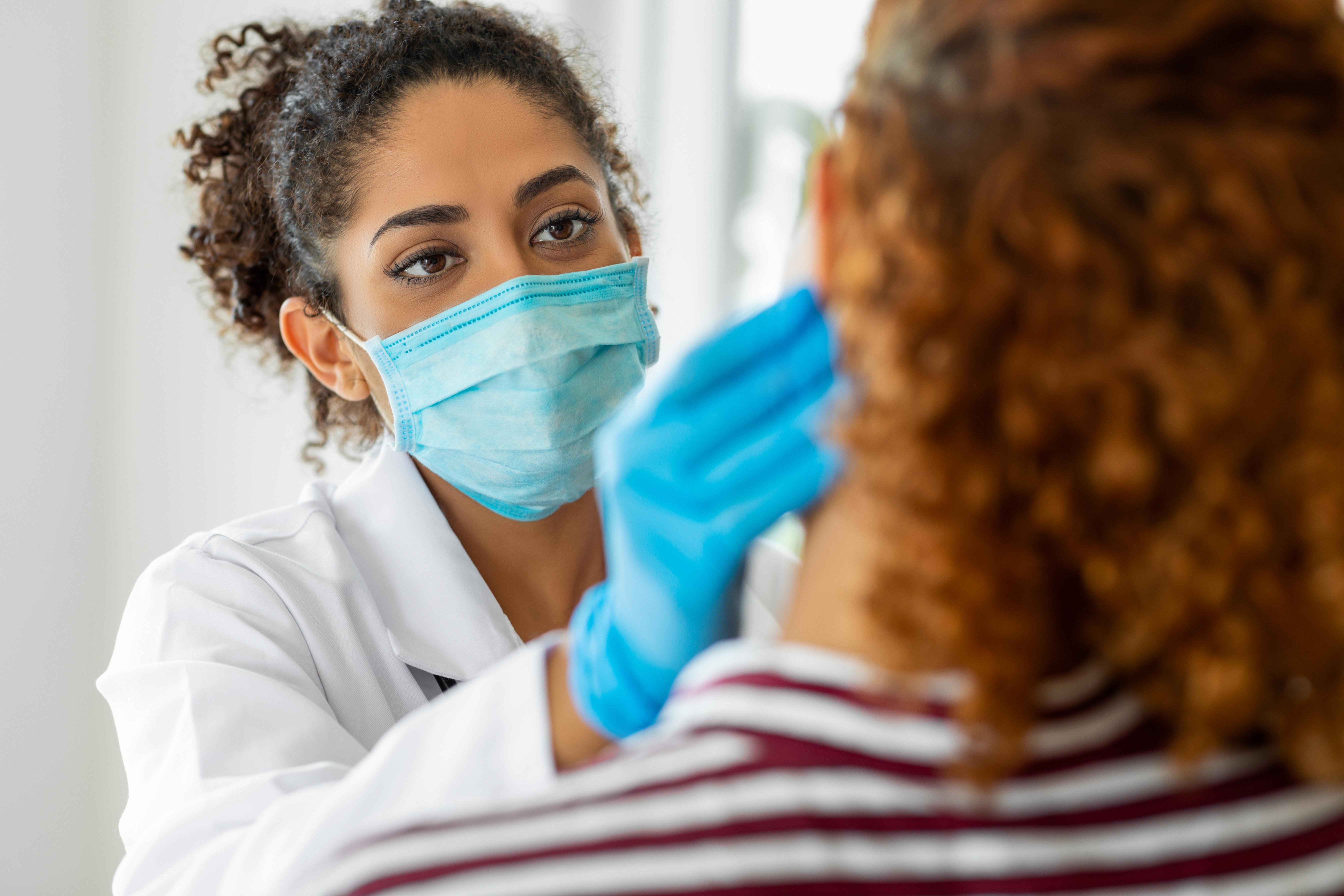 Doctor wearing a mask and gloves examines a patient.