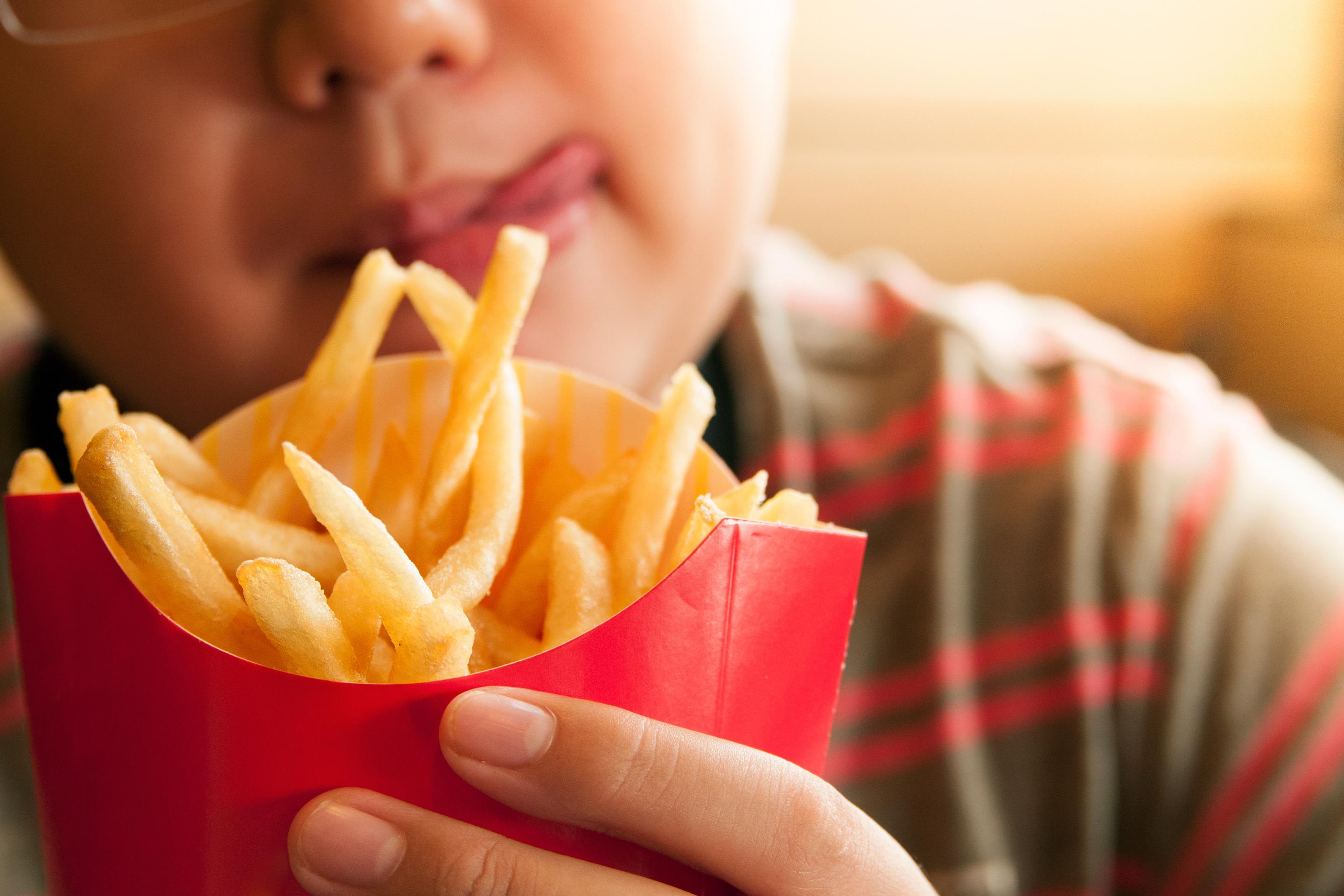 A young boy holds a red open co<em></em>ntainer filled with french fries.
